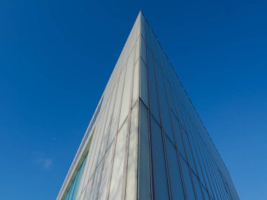 Camdan yüksek açılı bir binanın dramatik alçak açılı görüntüsü derin mavi gökyüzüne karşı keskin bir geometrik köşe oluşturuyor. Kopya alanı olan modern mimari arkaplan.