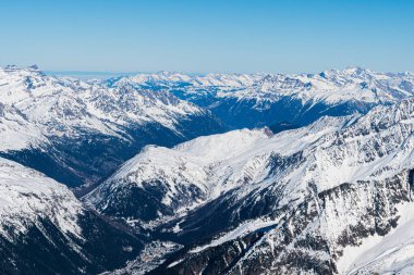 Açık mavi gökyüzünün altındaki Alp dağlarının geniş panoramik manzarası. Engebeli tepeleri, derin vadileri ve el değmemiş karlı kış manzaraları seyahat, doğa, macera ve iklim kavramları için idealdir.