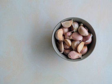 Nötr dokulu arka planda seramik bir kaseye yerleştirilmiş kaliteli sarımsak karanfillerinin üst görüntüsü. Doğal yumuşak ışığı olan minimalist mutfak kompozisyonu, gurme yemekleri, sağlıklı beslenme ve tarladan sofraya konseptler için ideal.
