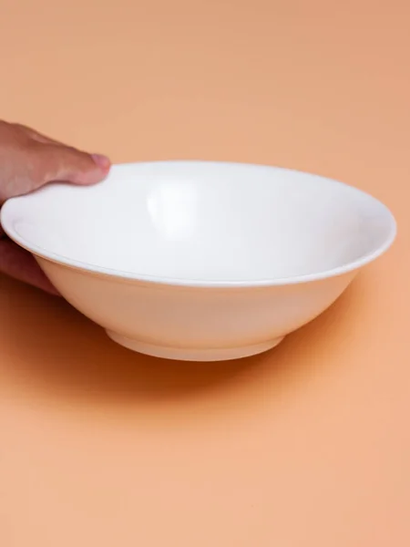 Kadın eli turuncu arka planda beyaz bir kase tutuyor. Yan görünüm.