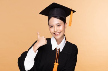 Güzel, çekici Asyalı kadın kep ve cübbe tebessümü ile mezun oldu. Gurur ve mutluluk dolu, bej arka planda izole edilmiş, Eğitim Başarı Konsepti.