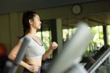 Koşu bandında ve spor salonunda koşan çekici genç Asyalı kadın sporcu çekici Asyalı kadın sporcu koşu bandında ve spor salonunda antrenman yapıyor.