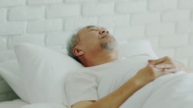 Asyalı yaşlı adam gözlerini kapatır gülümser uyur ve tatlı rüyalar görür yatak odasında sabah rahat ve rahat hissedersin sağlık ve uyku konsepti