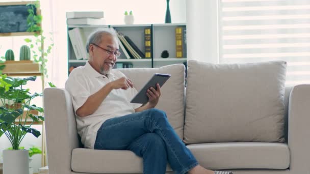 Lycka Äldre Asiatisk Man Sitter Soffan Och Använder Datorplatta Vdo — Stockvideo