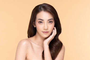 Güzel Asyalı genç bir kadın yumuşak yanaklı gülüşüne dokunuyor taze tenli mutlu ve neşeli, olumlu duygusal, bej arka planda soyutlanmış, güzellik estetiği ve yüz bakımı kavramında.