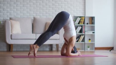 Çekici Asyalı kadının sakinliği yoga amuda kalkıp sabahları yatak odasında meditasyon yapıyor. Kendini çok rahat hissediyor ve evde dinleniyor, sağlık ve egzersiz yapıyor.