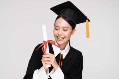 Güzel, Çekici Asyalı kadın, elinde sertifikası, gururu ve mutluluğu ile beyaz arka planda izole edilmiş, Eğitim Başarı Konsepti ile kep ve cübbe gülümsemesiyle mezun oldu.