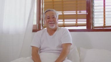 Mutlu Asyalı emeklilikler uyanın ve yeni bir gün doğarken rahat yatak odasında mutlu ve neşeli, sağlıklı yaşlı bir adam gülümseyin.