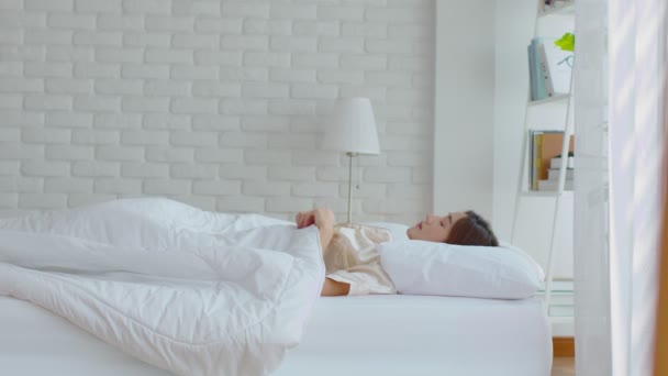 美しいアジアの若い女性が彼女の目を閉じますベッドの上に横たわって 居心地の良いベッドルームで眠ります快適で幸せ ヘルスケアコンセプト — ストック動画