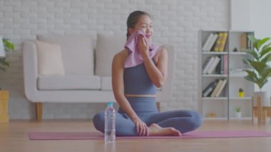 Asya 'lı sporcu kadının sağlığı yoga egzersizlerine ara verip evde taze enerji ve mutluluk için temiz su içmesi, rahat bir oturma odasında çalıştıktan sonra rahatça gülümseyen sağlıklı bir kadın.