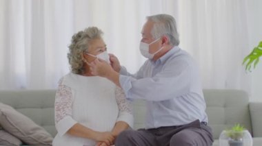Mutlu Asyalı yaşlılar ya da yaşlı çiftler tıbbi maske takarak evdeki oturma odasındaki kanepede oturan Coronavirus 'u engelliyor. 