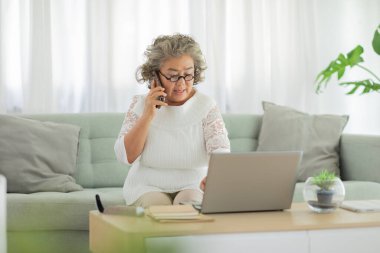 Beyaz saçlı yaşlı Asyalı kadın, bilgisayar sorunu veya insan hatası ile ilgili çözüme ulaşmak için cep telefonuyla müşteri hizmetleriyle konuşuyor. Emekliler yanlış ödeme ve teknolojiyle boğuşuyorlar. 