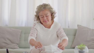 Mutlu Asyalı yaşlılar ya da tıbbi maske takan yaşlı kadınlar Coronavirus çapraz kollarını önlemek için evdeki oturma odasında kanepede oturuyorlar. 