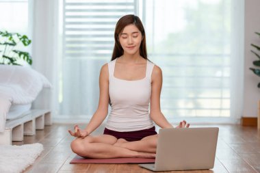 İyi Atletizm Atleti Asya Hintli kadın dizüstü bilgisayarı arayan yoga nilüferleri evde meditasyon ve rahatlama için poz veriyor, yoga egzersiz sınıfı konsepti, COVID-19 salgını nedeniyle kendini izole etme