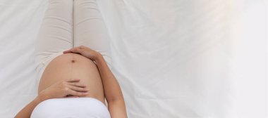 Üst tabaka Mutlu Hamile Kadın yatağında oturuyor ve koca karnını okşuyor, Genç kadının hamileliği gelecekten, annelikten ve gebelikten keyif alıyor, Boşluğu Kopyala