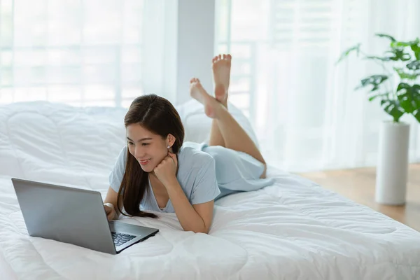 아름다운 아시아젊은 침대에 컴퓨터 랩탑을 사용하여 휴일에 침실에서 미디어와 쇼핑을 — 스톡 사진