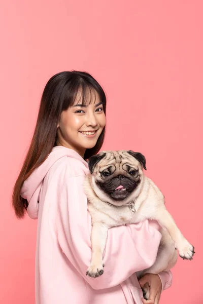 美人アジアの若いです女性保持犬パグ品種オン彼女の腕の笑顔と幸せ 所有者抱擁彼女の可愛いですペット犬とともに愛ピンクの背景 若いです女の子とともに可愛いです犬パグ品種見ますカメラ — ストック写真