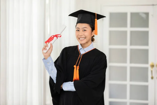 Asian graduate in cap and gown smile and holding certificate or diploma proud of yourself,Graduated young woman holding diploma happiness with success education,graduation celebration concept