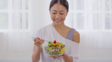 Sağlıklı genç Asyalı kadın sebze karışımı yiyor. Evde taze salata, elinde marul, domates, salatalık, cam kasede salatalık tutan gülen Hintli kadın vitamin, kalsiyum, folik, lifli yaşam sürüyor.