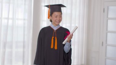 Şapka ve cübbe giymiş, gülümseyen, elinde sertifika ya da diplomayla gurur duyan, diplomasını başarıyla alan genç bir kadın, mezuniyet töreni konsepti.