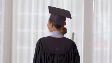 Şapka ve cübbe giymiş, gülümseyen, elinde sertifika ya da diplomayla gurur duyan, diplomasını başarıyla alan genç bir kadın, mezuniyet töreni konsepti.