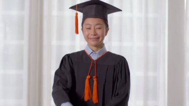 Şapka ve cübbe giymiş, gülümseyen, elinde sertifika ya da diplomayla gurur duyan, diplomasını başarıyla alan genç bir kadın, mezuniyet töreni konsepti.