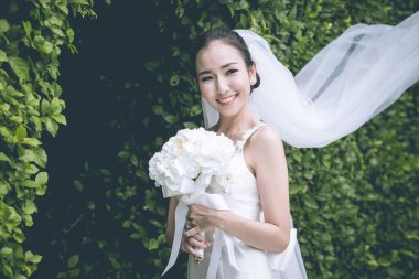 Güzel Asyalı gelin gelinlik giyip, gülümseyerek ve buket tutarak düğün gününde çok gururlu ve mutlu hissederek, Vintage Tone,