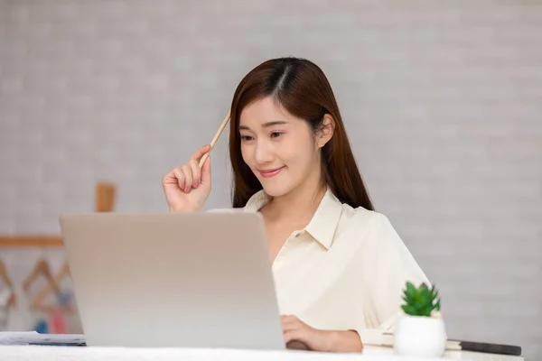 ビジネスアジアの若い女性がコンピュータのノートパソコンを持ってペンを保持し 自宅でそう幸福感中小企業のスタートアップの概念にアイデアや要件を得るために考えて — ストック写真