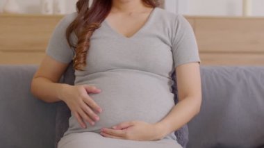 Mutlu Hamile Kadın koltukta oturup karnını okşuyor. Genç bir kadının gelecekten zevk alması evde rahatla. Hamilelik konsepti. Odaklan.