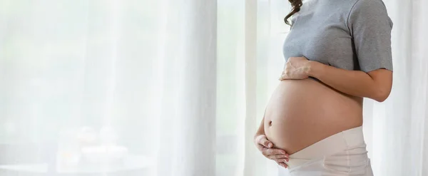 Sztandar Szczęśliwej Kobiety Ciąży Stoi Przed Oknami Głaskanie Duży Brzuch — Zdjęcie stockowe