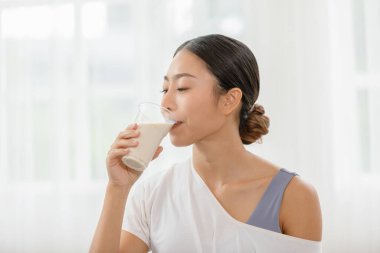 Sağlıklı genç Asyalı kadın evde güçlü kemik için kalsiyumlu süt içiyor, cam üzerinde soya sütü tutan gülümseyen Hintli kadın beslenme sağlıklı hayattan keyif alıyor, doğal süt tazeliğinden keyif alıyor.