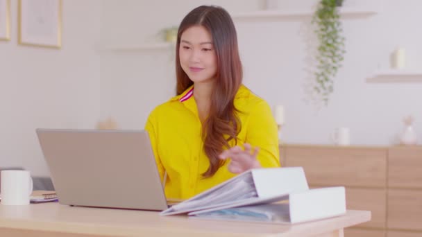ラップトップコンピュータを使用して美しい創造的なアジアの若い女性と彼女の仕事を参照するために開かれた文書 — ストック動画