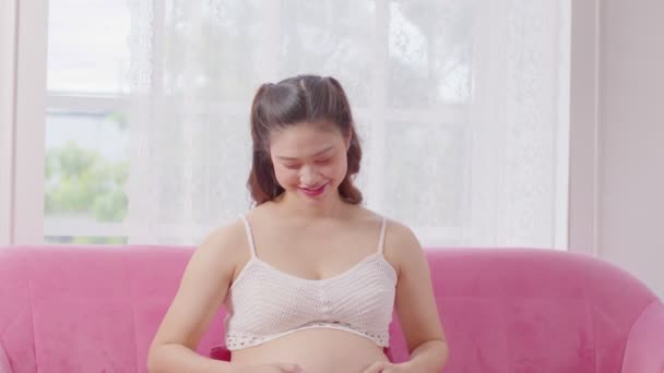 Счастливая Беременная Женщина Сидящая Розовом Диване Гладящая Свой Большой Животик — стоковое видео