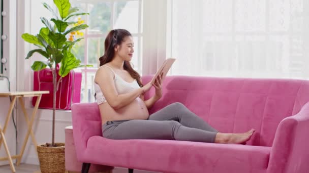 Ευτυχισμένη Έγκυος Γυναίκα Κάθεται Στον Καναπέ Κρατώντας Βιβλίο Και Ανάγνωση — Αρχείο Βίντεο