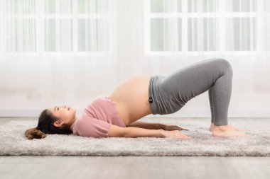 Hamile Asyalı genç kadın yoga ile meditasyon yapıyor. Yarı Köprü pozu veriyor. Yoga yapıyor. Genç sağlıklı hamile bir kadının meditasyonu.