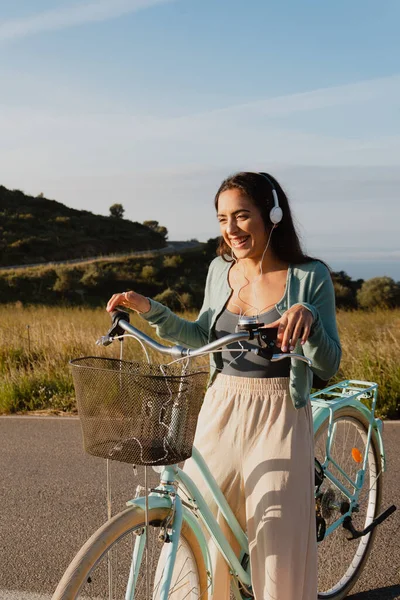 Smiling white woman listening to music with headphones riding a light blue bicycle