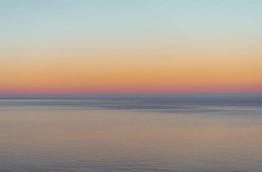 Gün batımının kırmızı, turuncu ve mavi renklerini bozan bir deniz ufku.