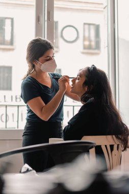 Makyöz bir mankenle işini yapıyor. Doğal ışığı olan bir pencerenin yanındaki evin içinde.