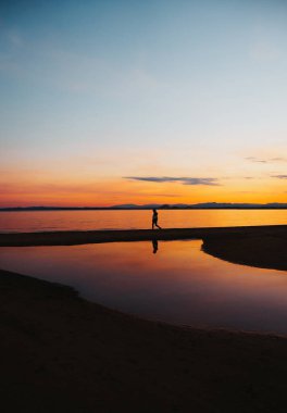 Denizde gün batımını seyrederek sakince yürüyen bir insan.