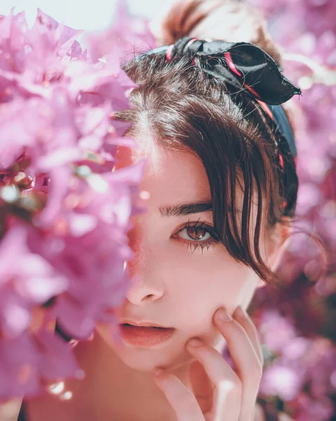 Kadının yüzü, eli yanağında pembe çiçeklerin arasında poz veriyor.