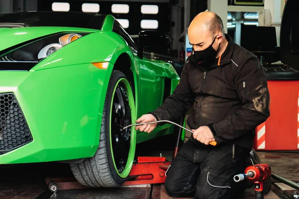 Tamirci üst düzey bir süper spor arabanın tekerlerini değiştiriyor. Otomobil tamircisi garajda çalışıyor. Onarım servisi.