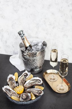 Şampanya kadehleri, köpüklü şarap ve istiridyelerin yanındaki kovada şişe.