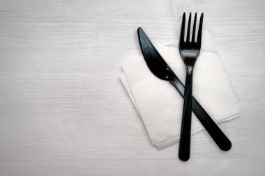 Siyah plastik çatal bıçak beyaz bir peçetede beyaz bir masa arkasında.