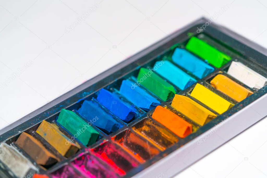 pastel art materials, crayons of different colors in a box on a white paper background