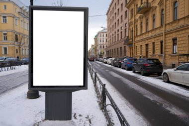 Beyaz alan MOCKUP ile dikey şehir reklam panosu. Öğleden sonra şehir merkezinde. Kışın açık hava reklamında kar yağarken.