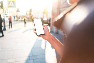 Bir adamın elinde çerçevesiz bir akıllı telefon vardır. Beyaz ekran telefonuyla işlek bir cadde modelinde.