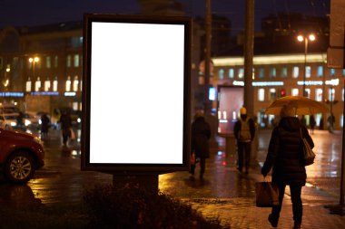 Billboard reklamı, gece şehrinde parlıyor. Reklamcılık için beyaz bir alan. İnsanlar arka planda sokakta gezinirken....