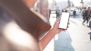 Bir adamın elinde çerçevesiz bir akıllı telefon vardır. Beyaz ekran telefonuyla işlek bir cadde modelinde.