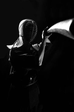 A kendo fighter sticking a wooden sword forward in an attacking position. Black and white photo In the dark key clipart