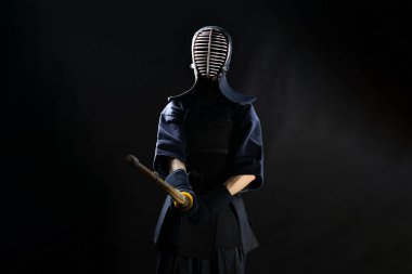 Kendo fighter in armor practicing with bamboo sword bokuto on black background clipart